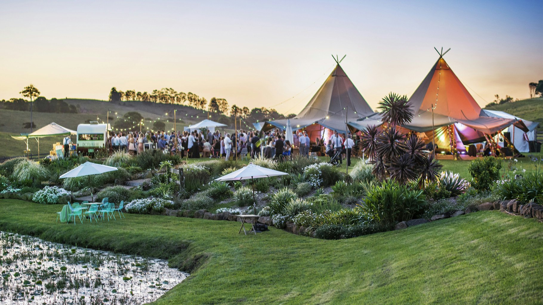 Tipi wedding reception at sunset with guests under festoon lighting.